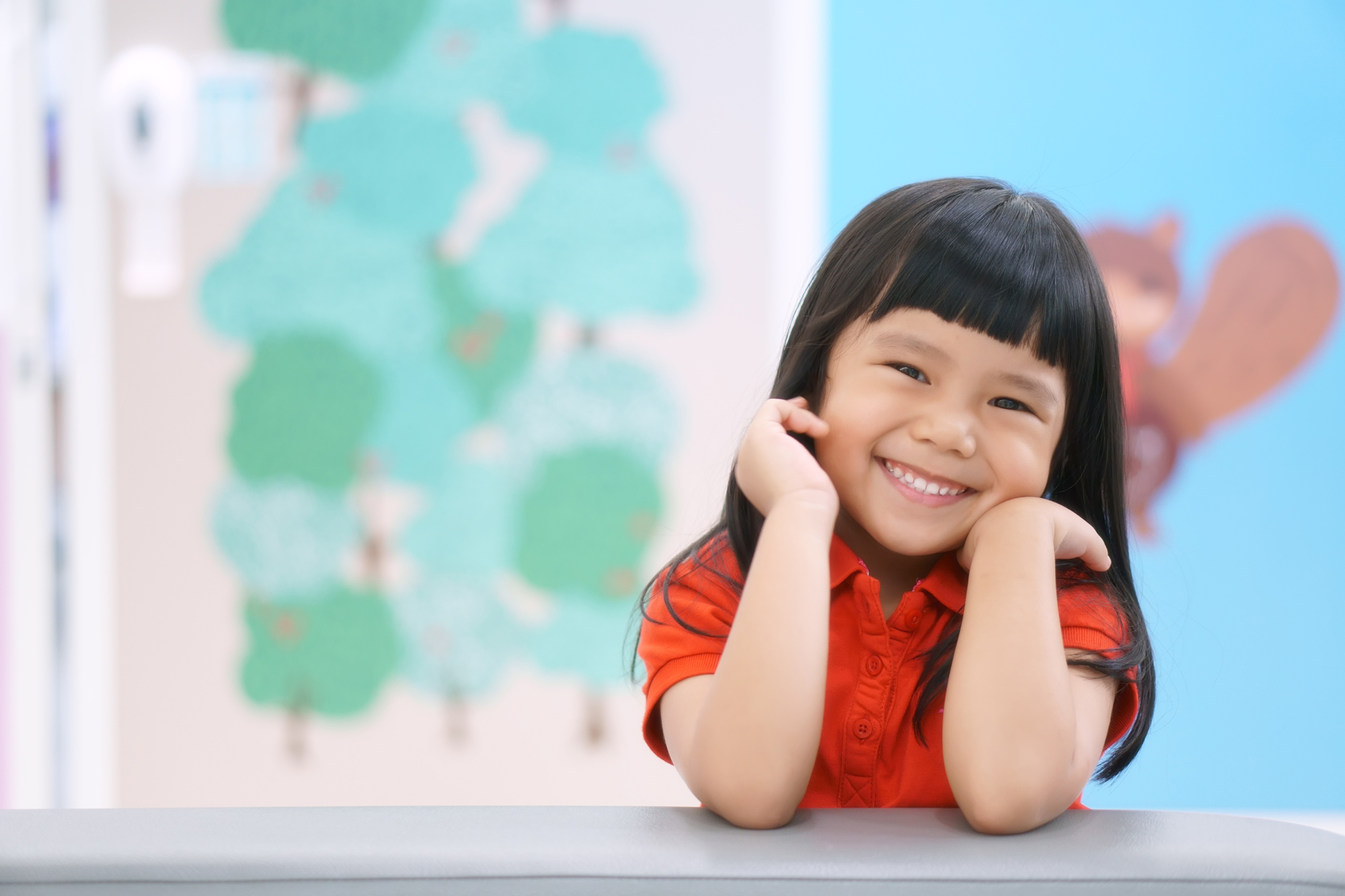 Asian girl child happy with a smile wearing red shirt leaning on sofa at preschool