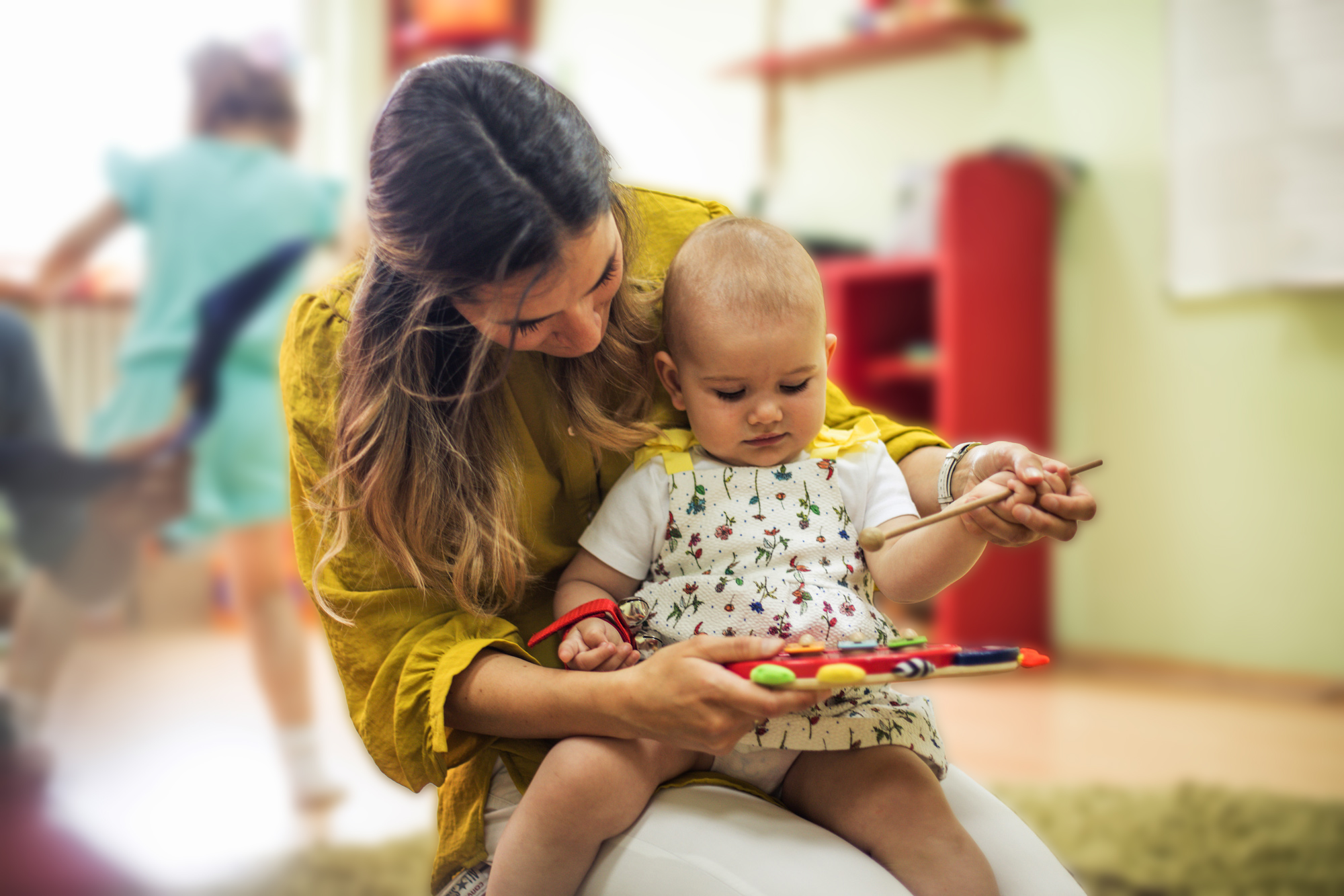 adult teacher with infant on lap playing with a toy in daycare setting