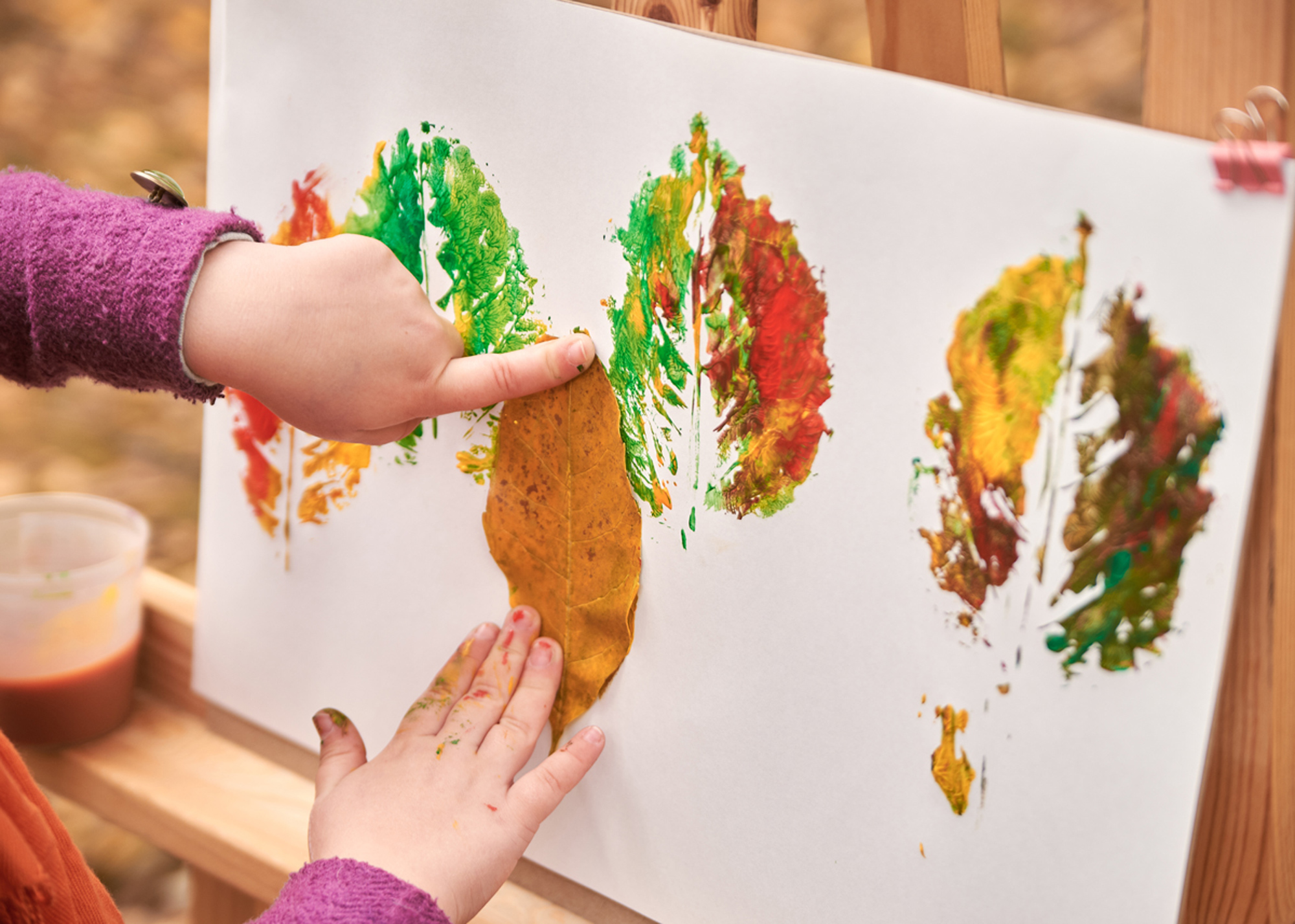 little girl artist paints autumn leaves in the park