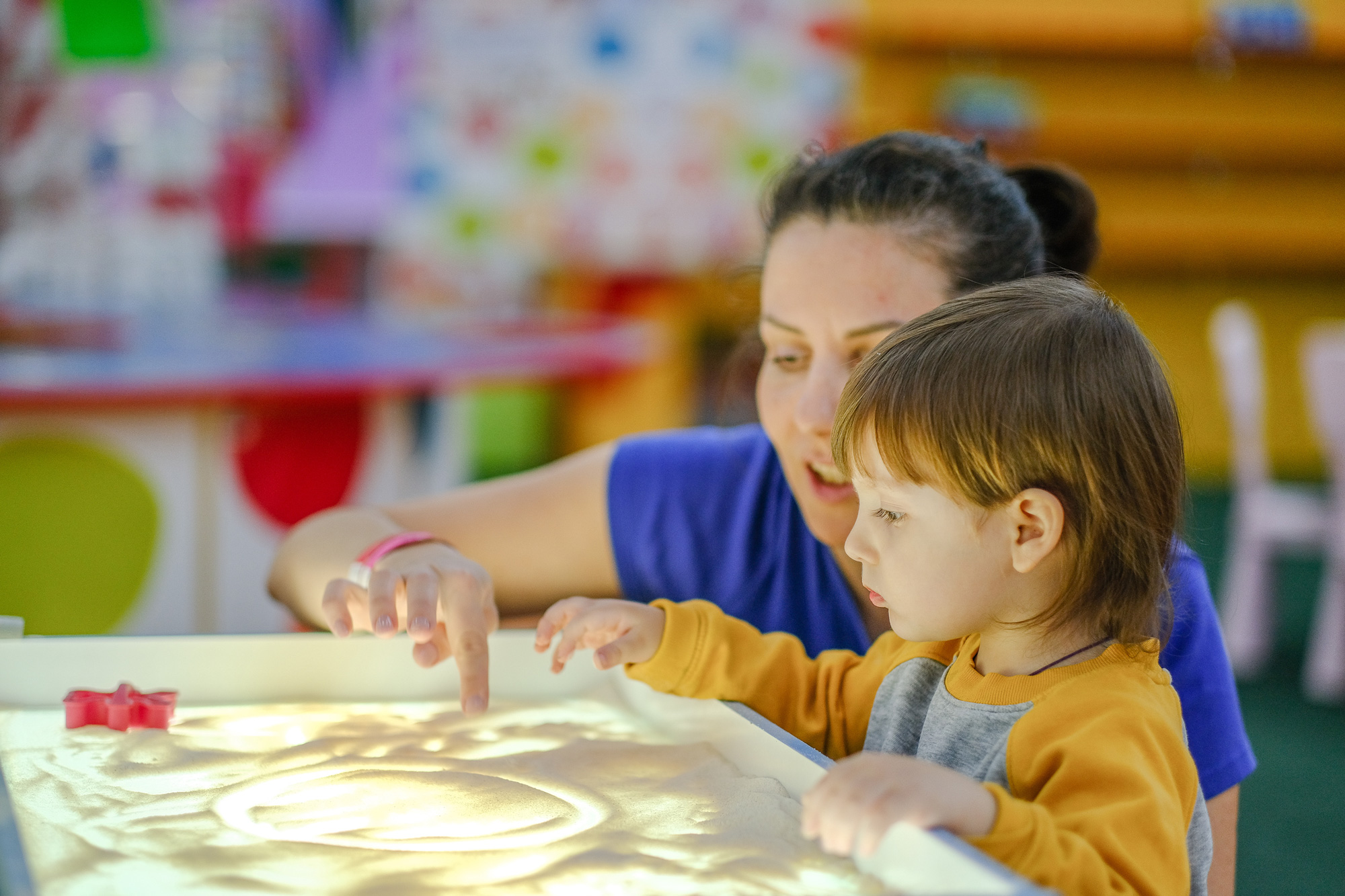 Creative early baby development. A teacher with her child to draw with her fingers in the sand