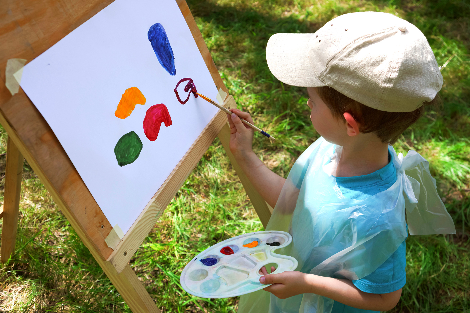 boy 3-4 years old draws on an easel with paints outdoors
