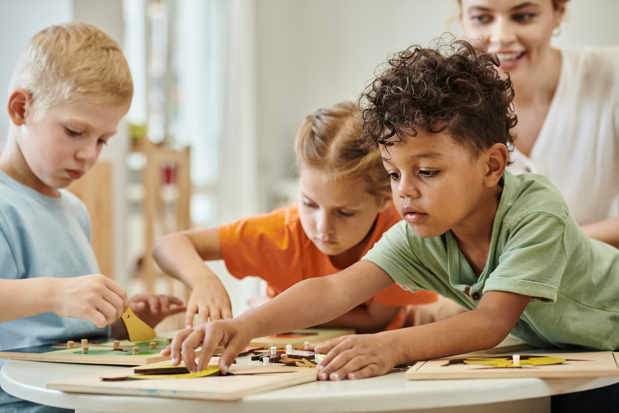toddler kids playing with puzzles at a table with teacher in montessori school